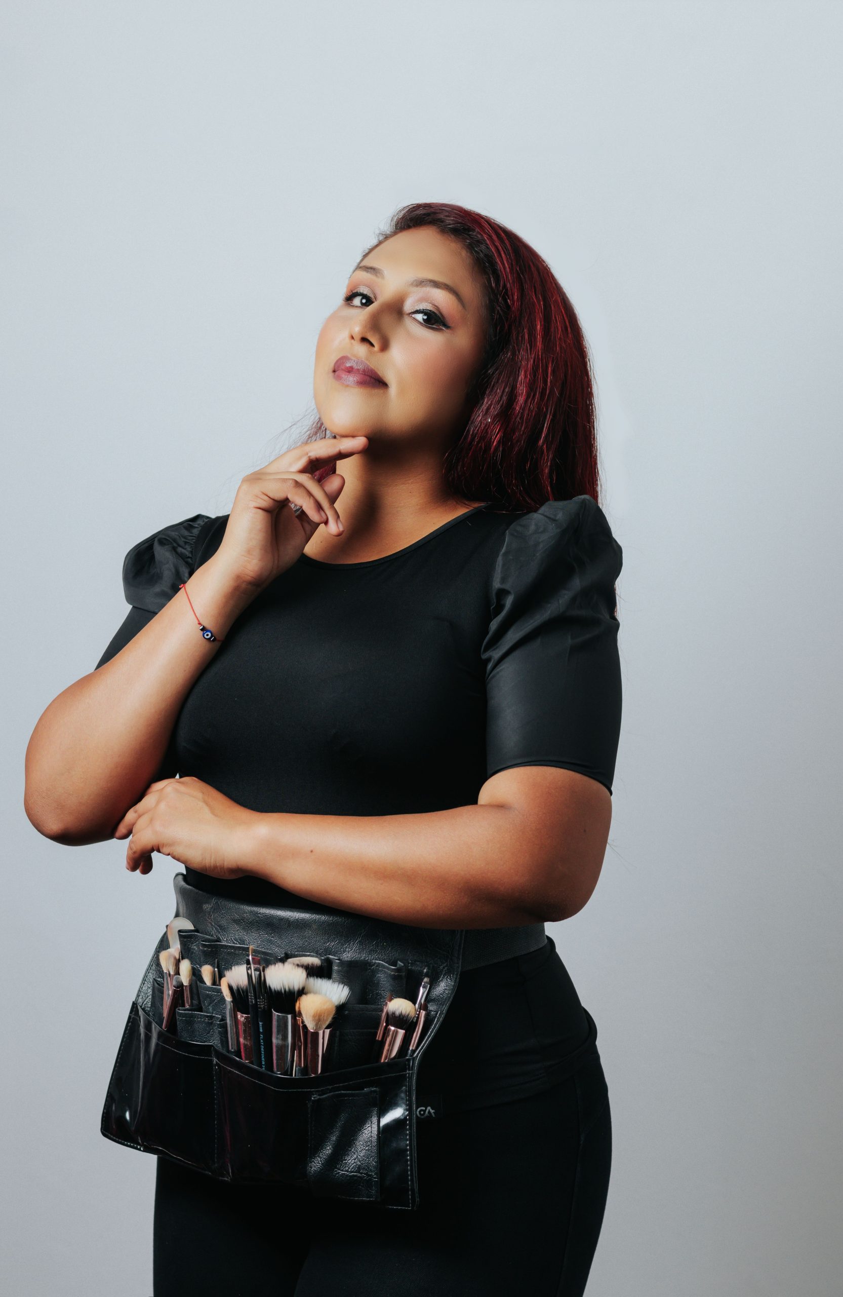 Portrait of a confident makeup artist with brushes, shot in a studio setting.