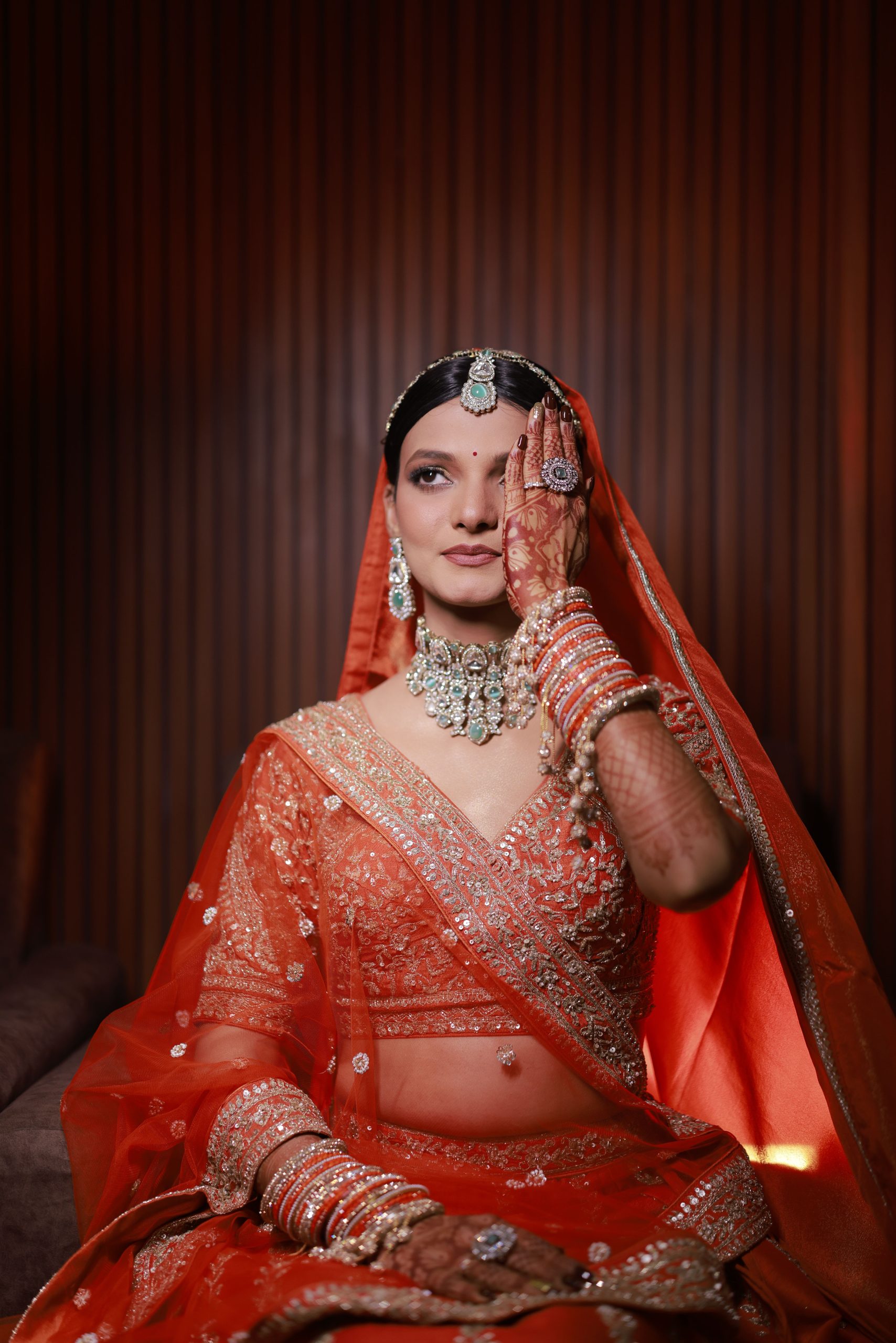 Stunning Indian bride in vibrant red attire with dazzling jewelry, posing indoors.
