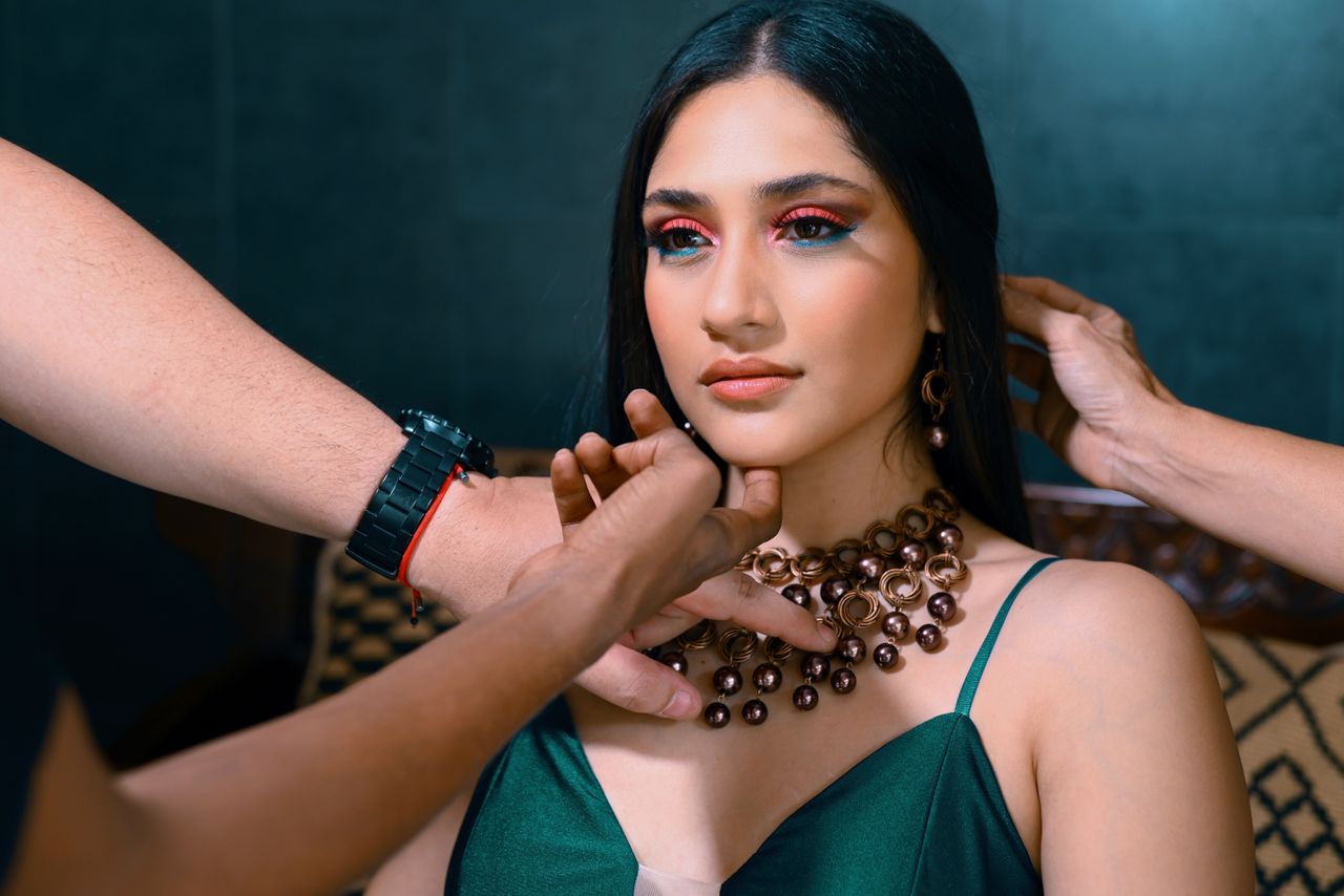 A fashionable woman being prepared for a photoshoot, adorned with elegant jewelry and makeup.