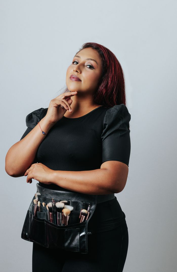Portrait of a confident makeup artist with brushes, shot in a studio setting.