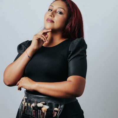 Portrait of a confident makeup artist with brushes, shot in a studio setting.
